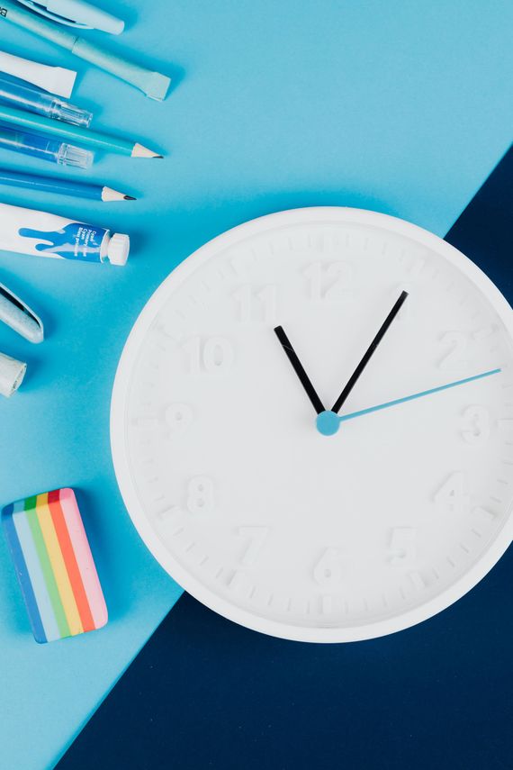White clock on blue desk with pens and erasers, viewed from above