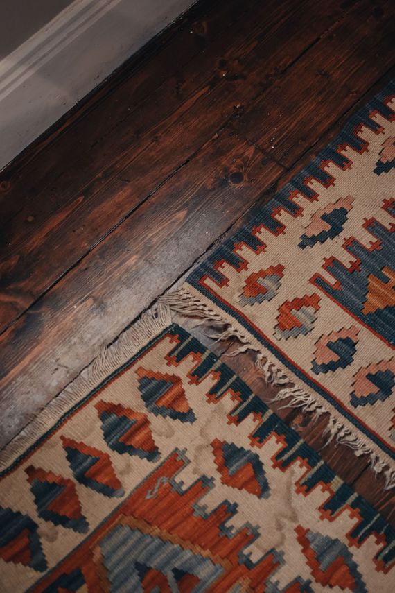 Wooden floor beside a patterned rug with geometric red, blue, and beige designs