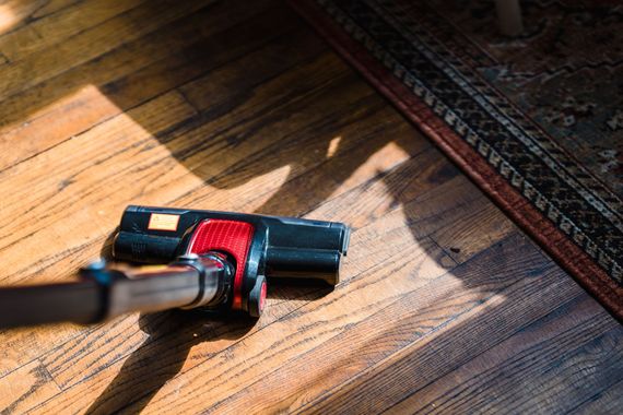 Cleaning tool on a wooden floor near a patterned rug, in sunlight