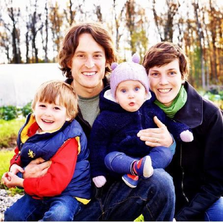 Family of four sitting outdoors, smiling in winter clothes, with trees in the background