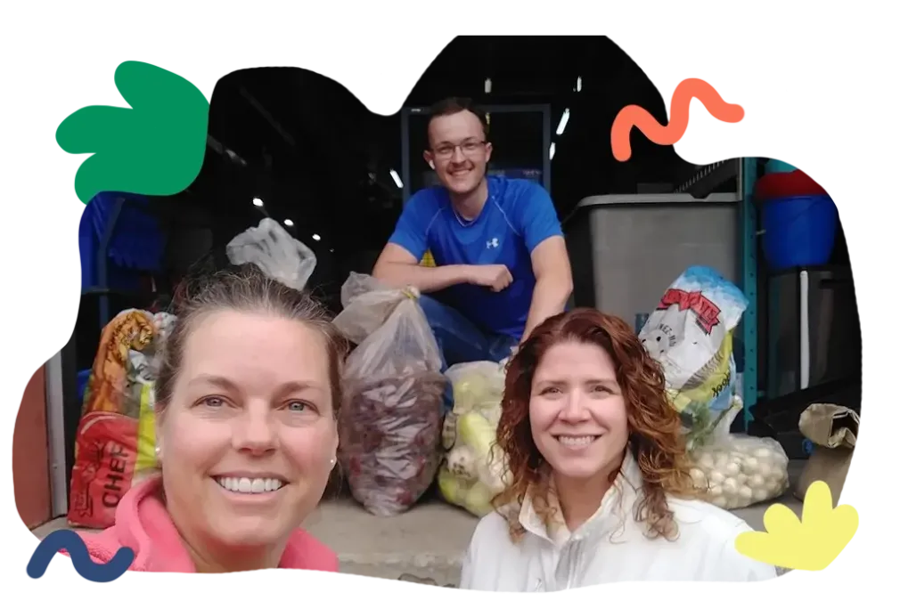Three people posing in front of bags of produce at a market stand