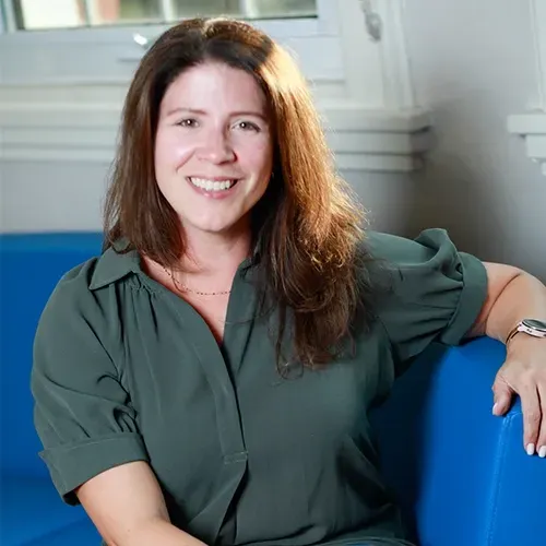 Smiling woman in a green blouse seated on a blue chair in a bright room