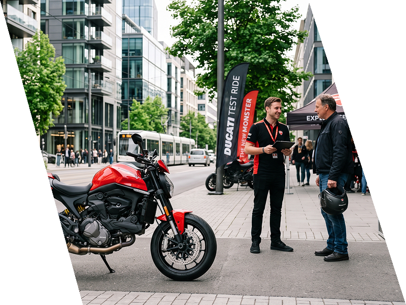 Uma motocicleta vermelha estacionada na calçada, ao lado de dois homens conversando, perto de prédios modernos.