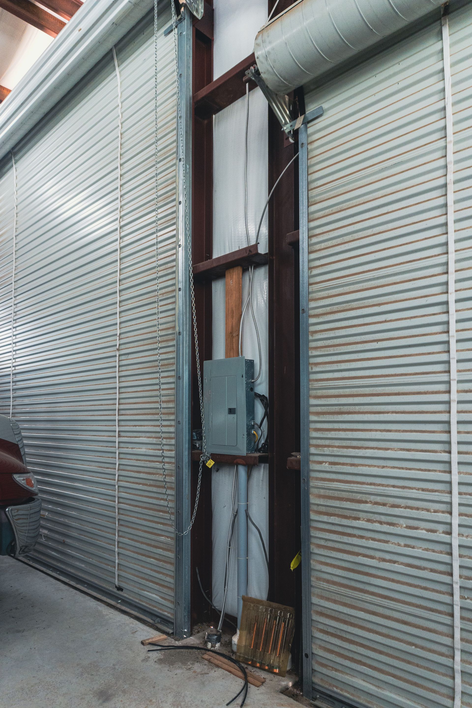 Metal roll-up doors with a utility box and cables mounted between them, in an industrial alley