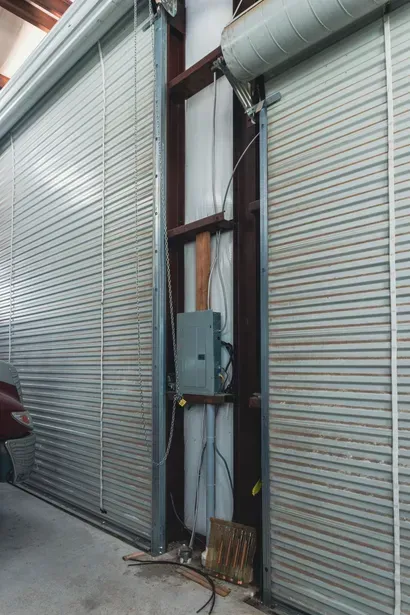 Roll-up metal doors with a narrow central service panel and electrical box in an industrial alley