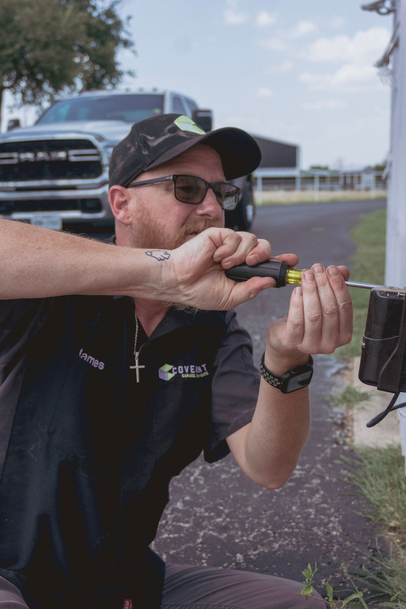 Man using a screwdriver to adjust a metal fixture outdoors near a parked truck