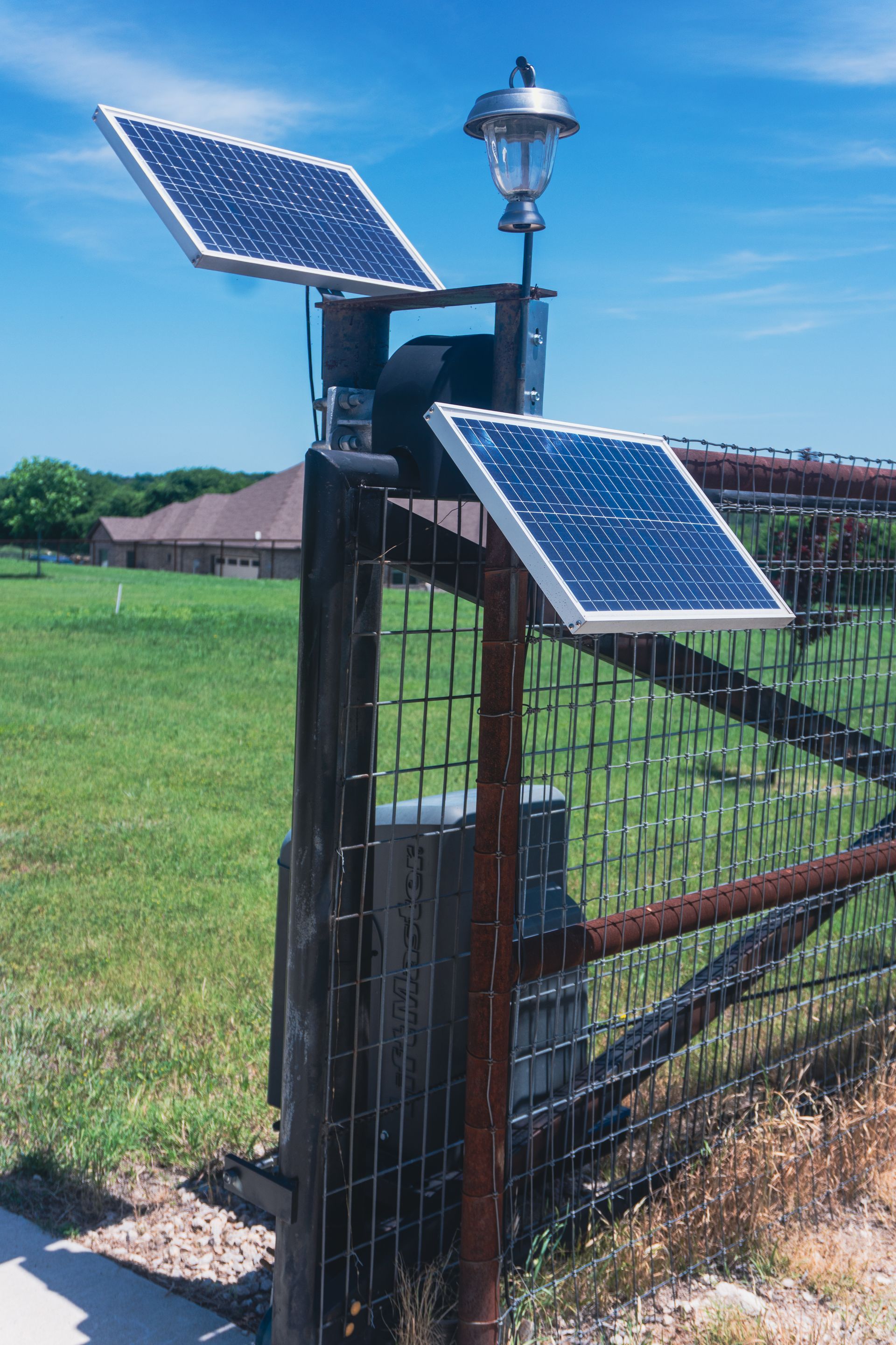 Solar-powered gate sensor with two panels mounted on a black fence in a grassy field