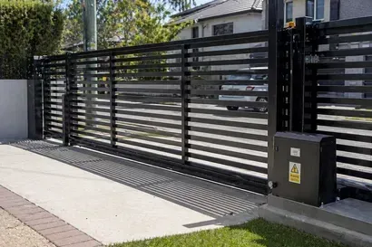 Black sliding metal gate beside a sidewalk and grass in front of a house