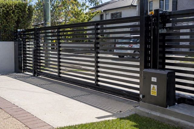 Black sliding metal gate beside a sidewalk and grass in front of a house