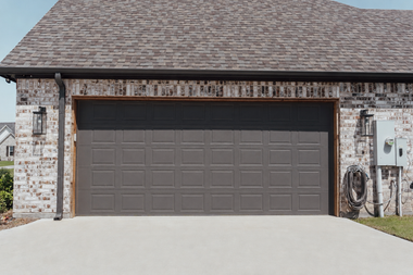 Red metal building with a large gray roll-up garage door and gravel foreground.