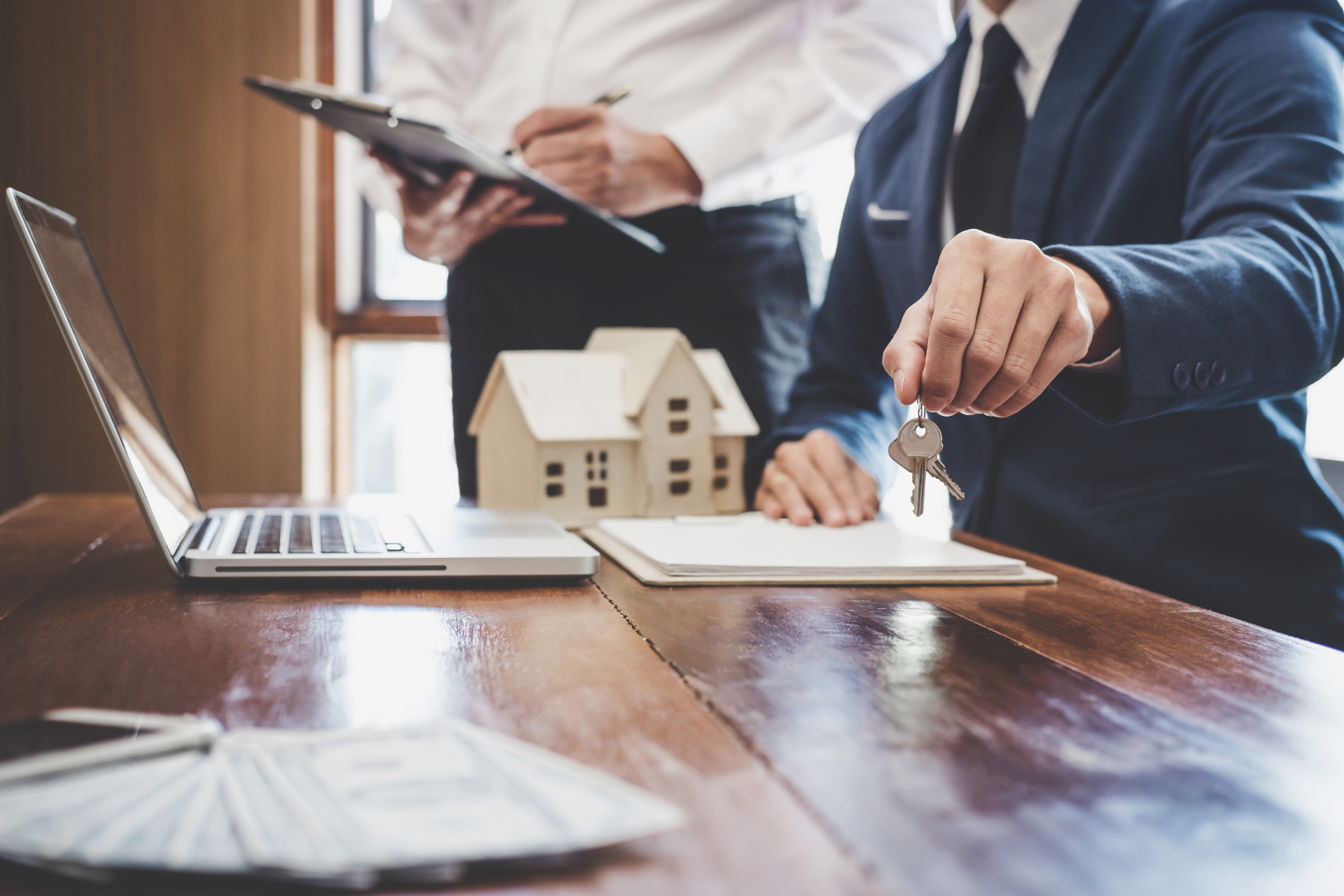 Real estate agents reviewing a house model and keys at a desk with a laptop and documents