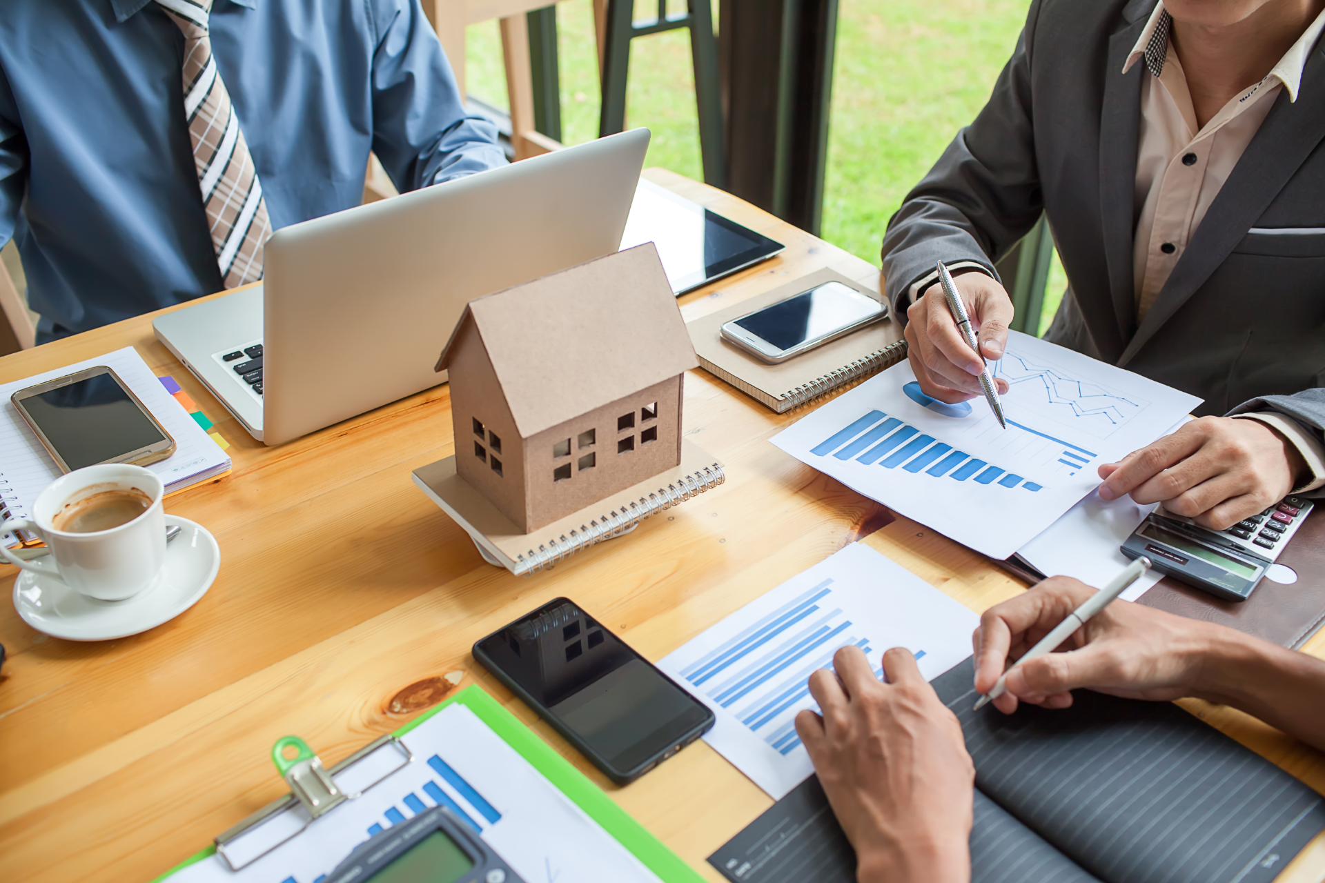 Team meeting with laptop, paperwork, tablet, and a small house model on a conference table
