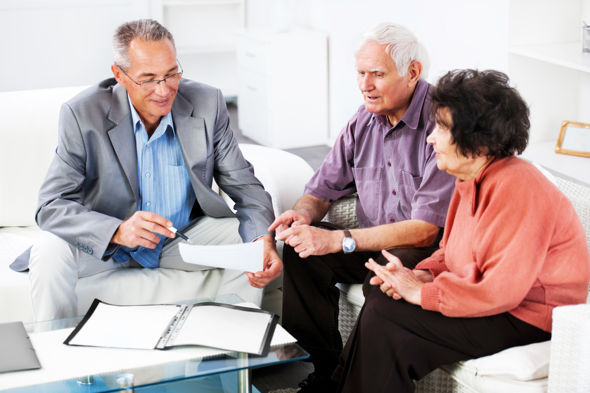 Three people in a bright living room discussing documents at a glass coffee table
