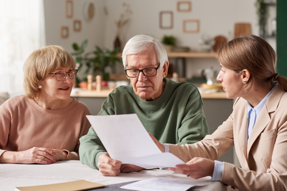 Three people discuss documents at a table in a bright office setting.