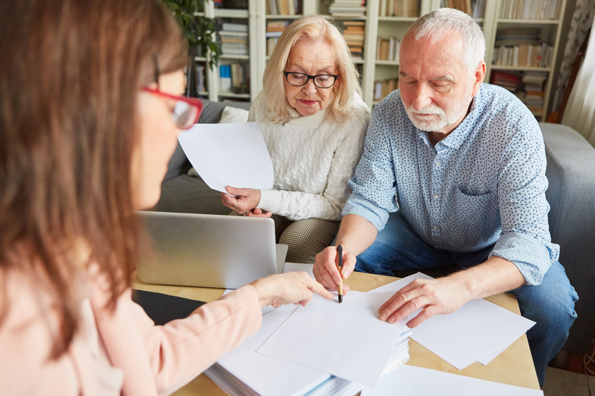 Three people reviewing paperwork at a table with a laptop in a home office