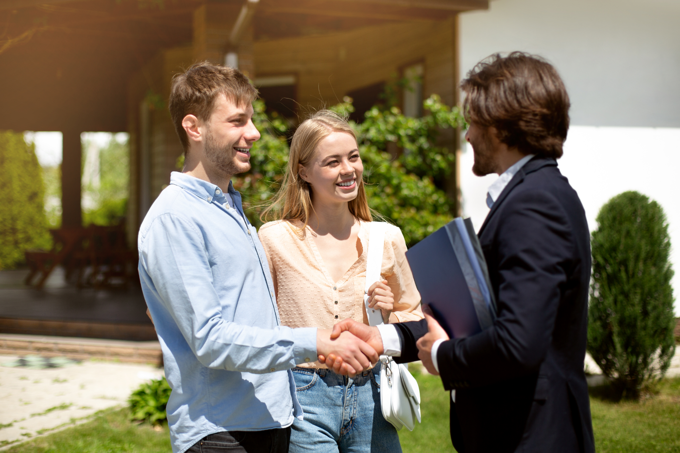 Two people shaking hands with a businesswoman outdoors in front of a building