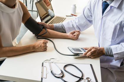 Blood pressure check at a clinic, with a cuff on a patient's arm and a doctor using a monitor.