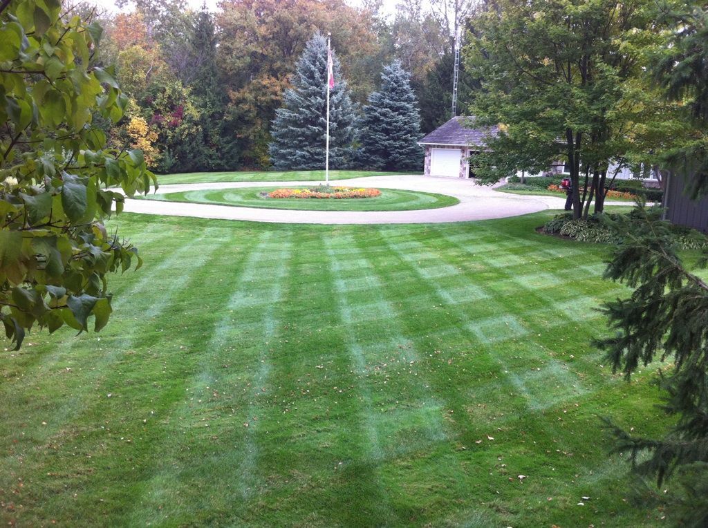 A lush green lawn in front of a house with a flag pole in the middle.