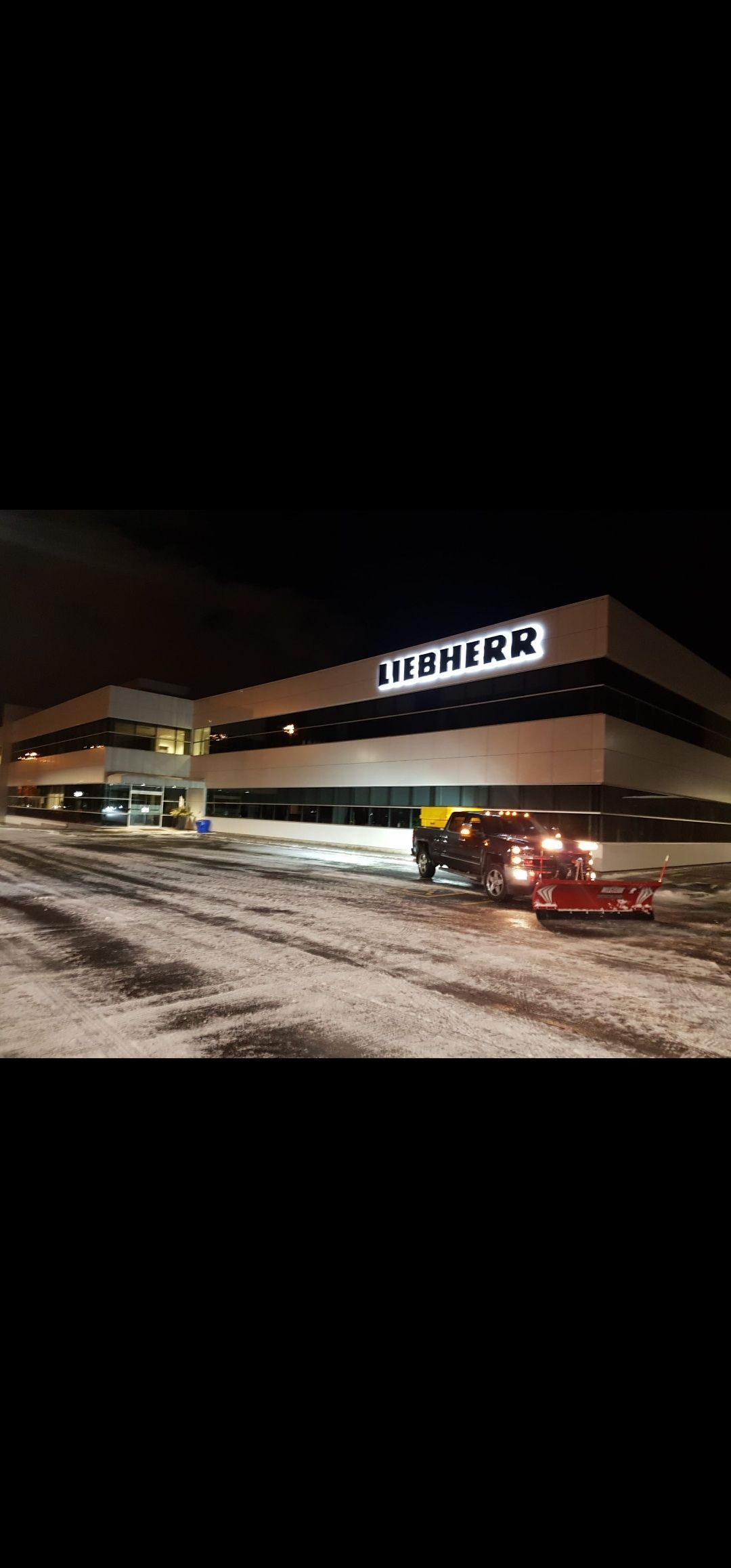 A modern building lit up at night with a red truck parked in front, on snow-covered ground.