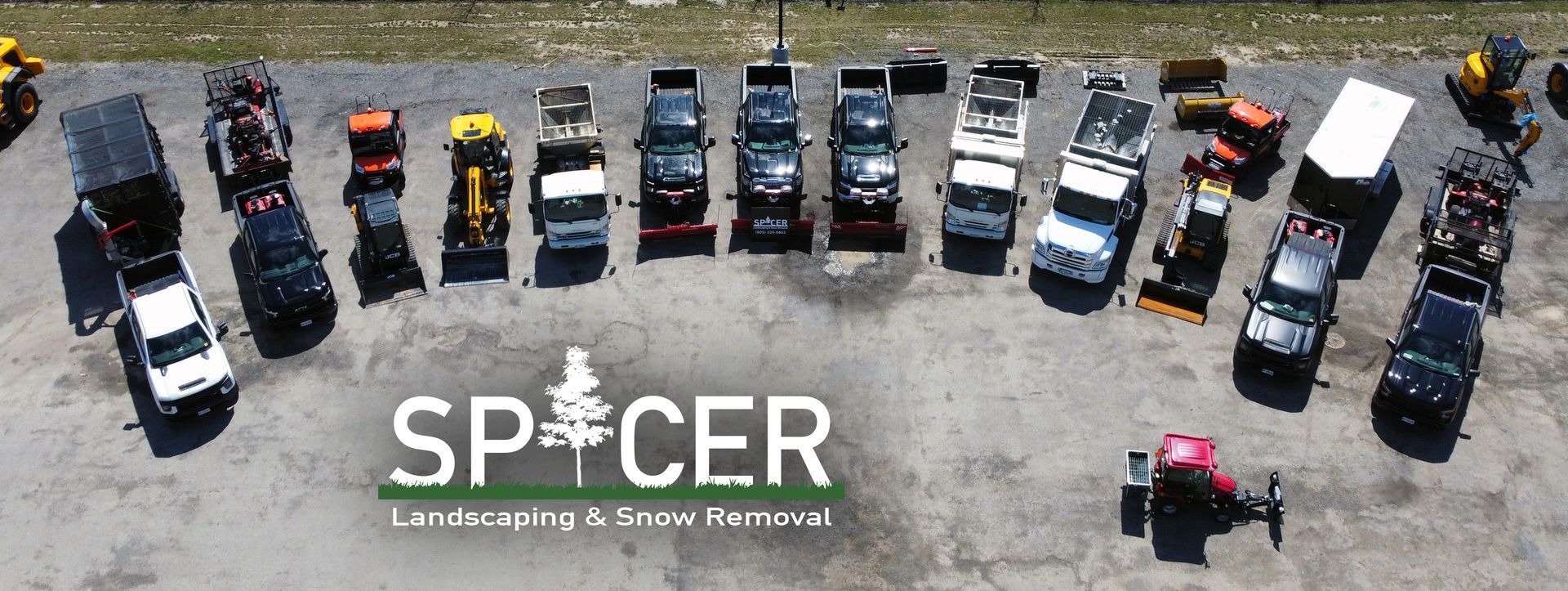 Aerial view of a fleet of snow removal and landscaping vehicles lined up in a gray parking lot.