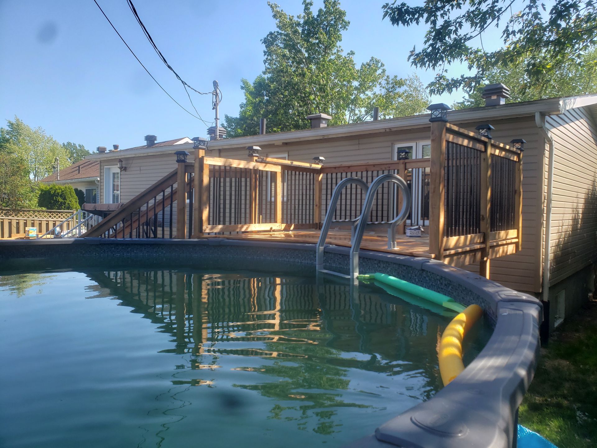 Une grande piscine devant une maison avec une terrasse en bois