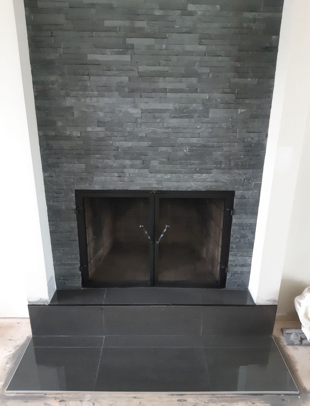 Une cheminée avec un sol en carrelage noir et un mur en briques noires.