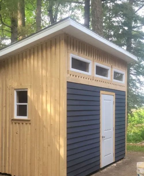 Un hangar en bois avec un revêtement noir et une porte blanche