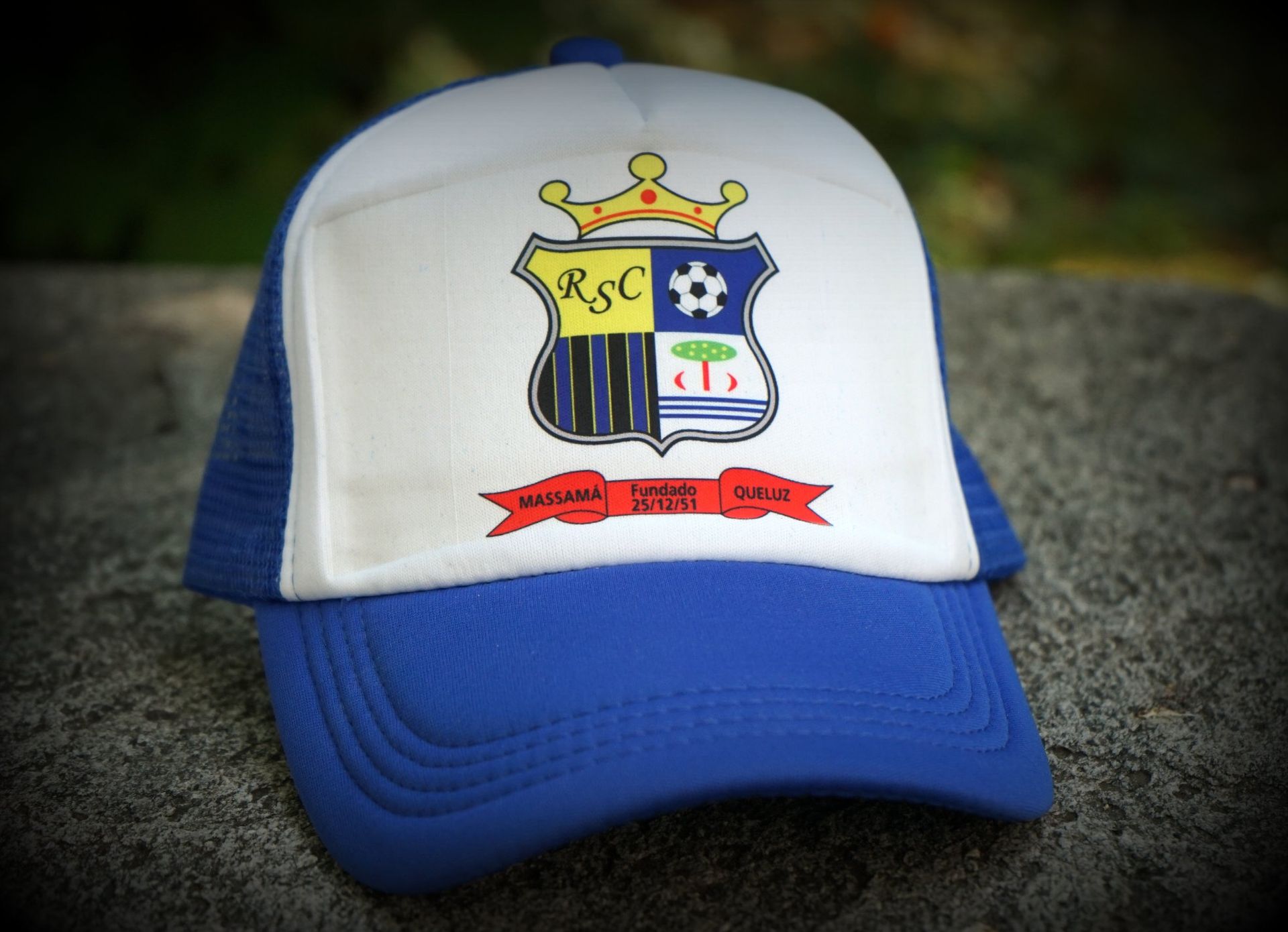 Casquette de baseball bleue et blanche avec un logo en forme d'écusson et un ruban rouge sur le devant