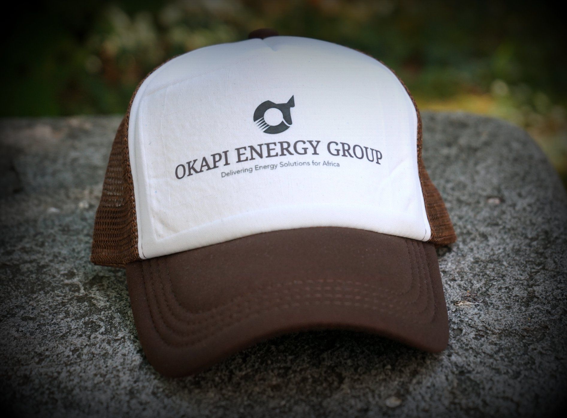 Casquette de camionneur marron et blanche avec le logo « OKAPI ENERGY GROUP » sur un rocher à l'extérieur