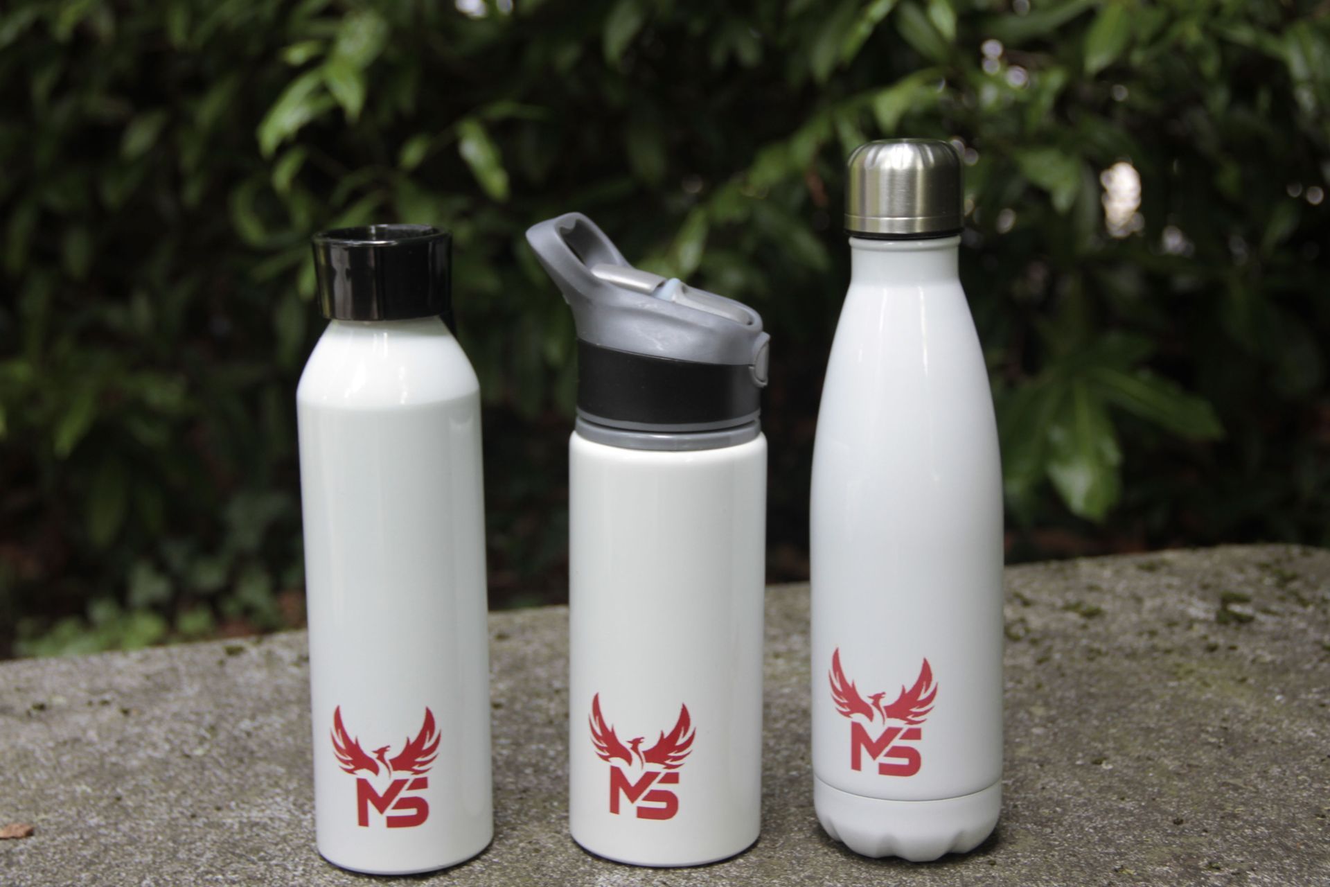 Trois bouteilles d'eau blanches avec des logos rouges posées sur une surface en pierre à l'extérieur
