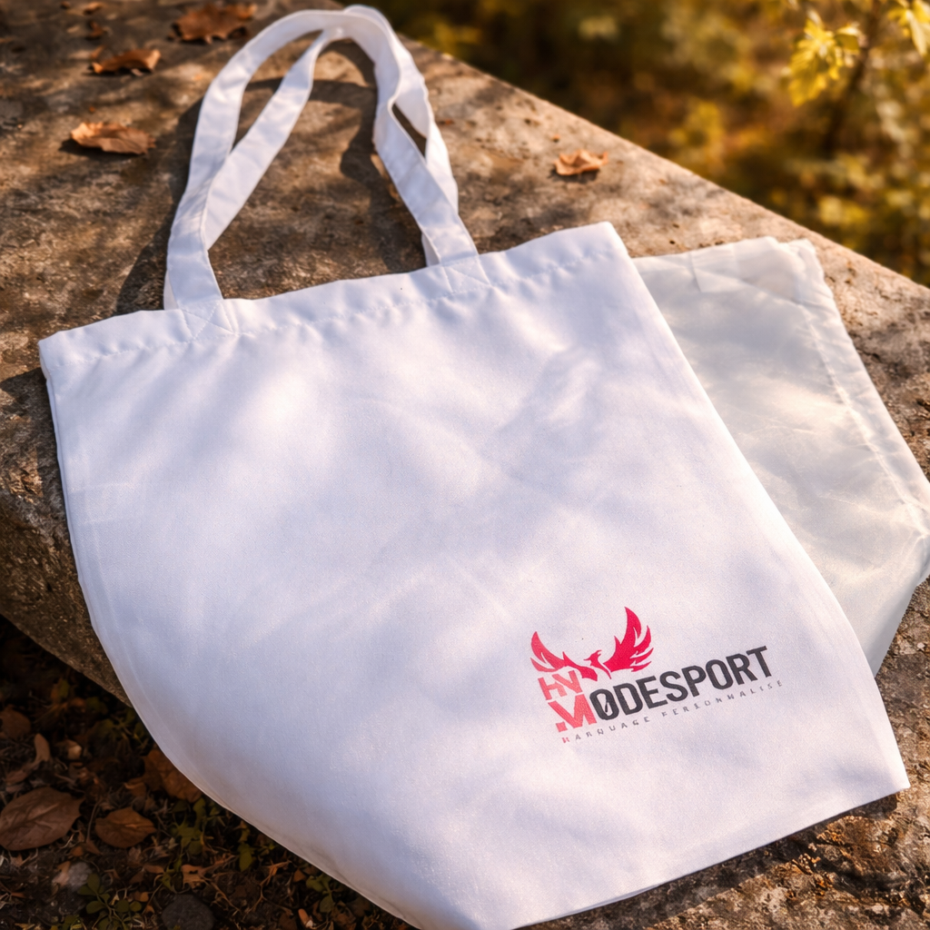 Sac cabas blanc à anses et logo rouge, posé sur une surface extérieure automnale.