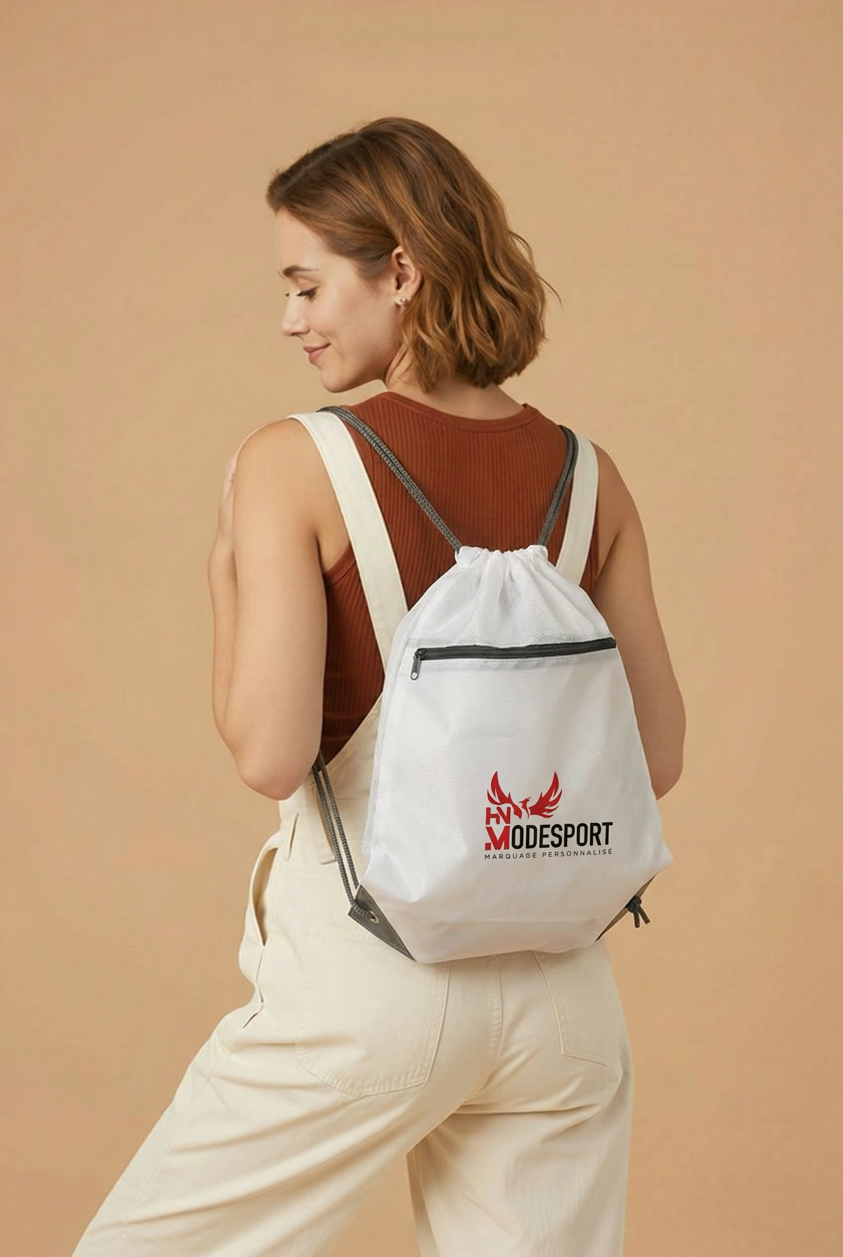 Femme portant un sac à dos blanc sur fond beige, légèrement tournée de profil.