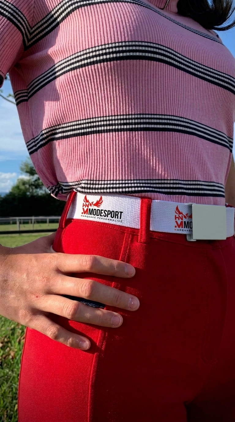 Personne vêtue d'une chemise à rayures roses et d'un pantalon rouge avec une ceinture blanche, la main sur la hanche, à l'extérieur.