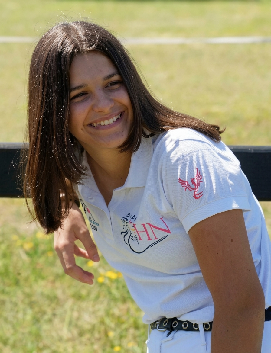 Une femme souriante en t-shirt blanc assise dans l'herbe, baignée de soleil.