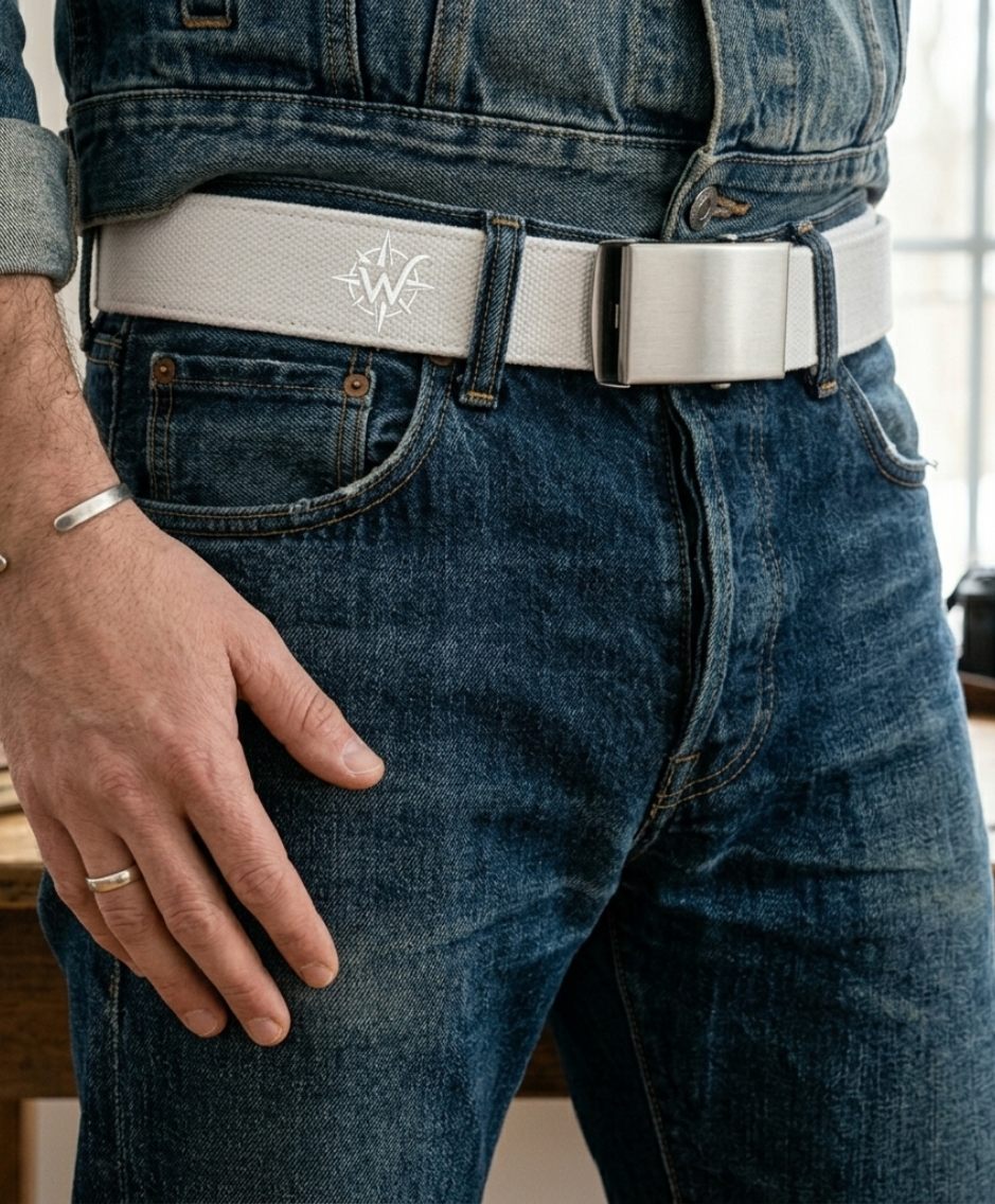 Gros plan sur un jean bleu avec une ceinture à boucle argentée et une main posée sur le côté