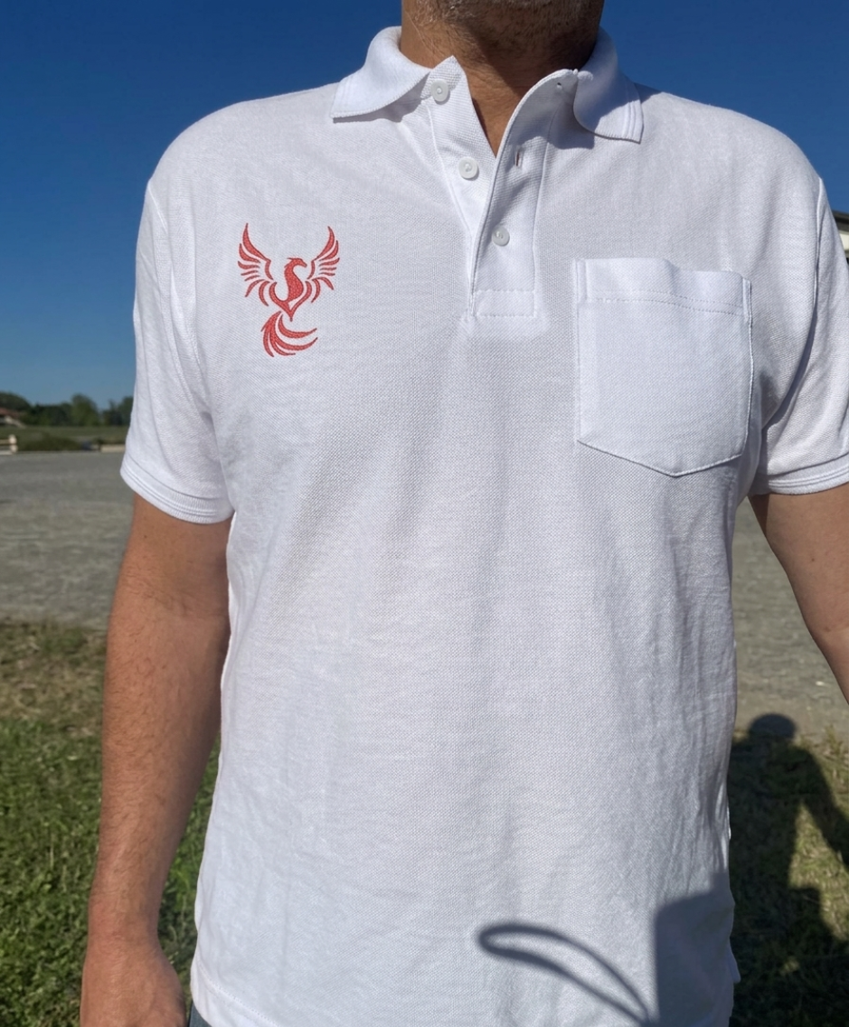 Une personne portant un polo blanc orné d'un logo d'oiseau rouge se tient à l'extérieur sous un ciel bleu.