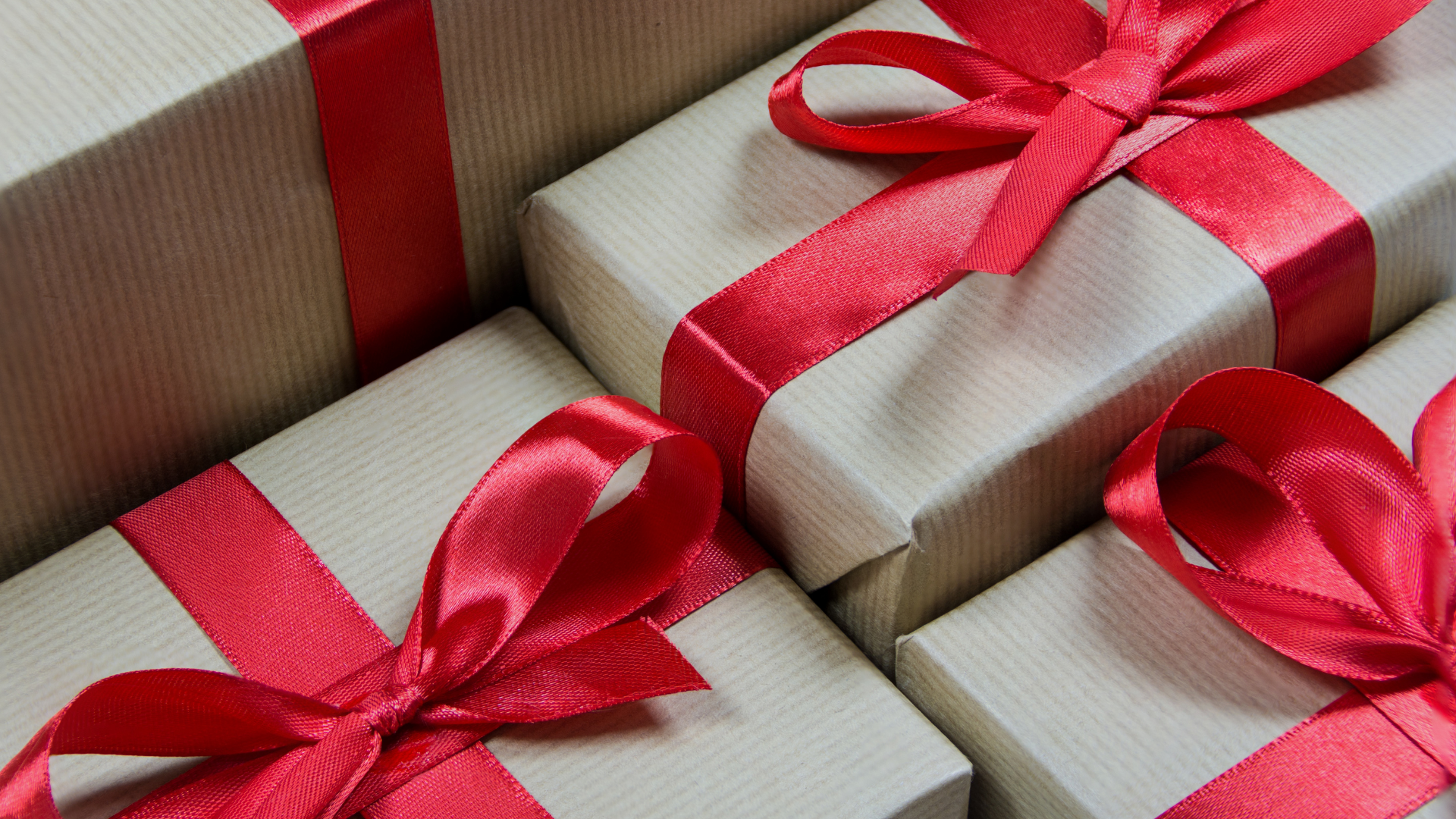 Boîtes cadeaux emballées dans du papier beige, des rubans marrons et des nœuds et rubans rouges vifs.