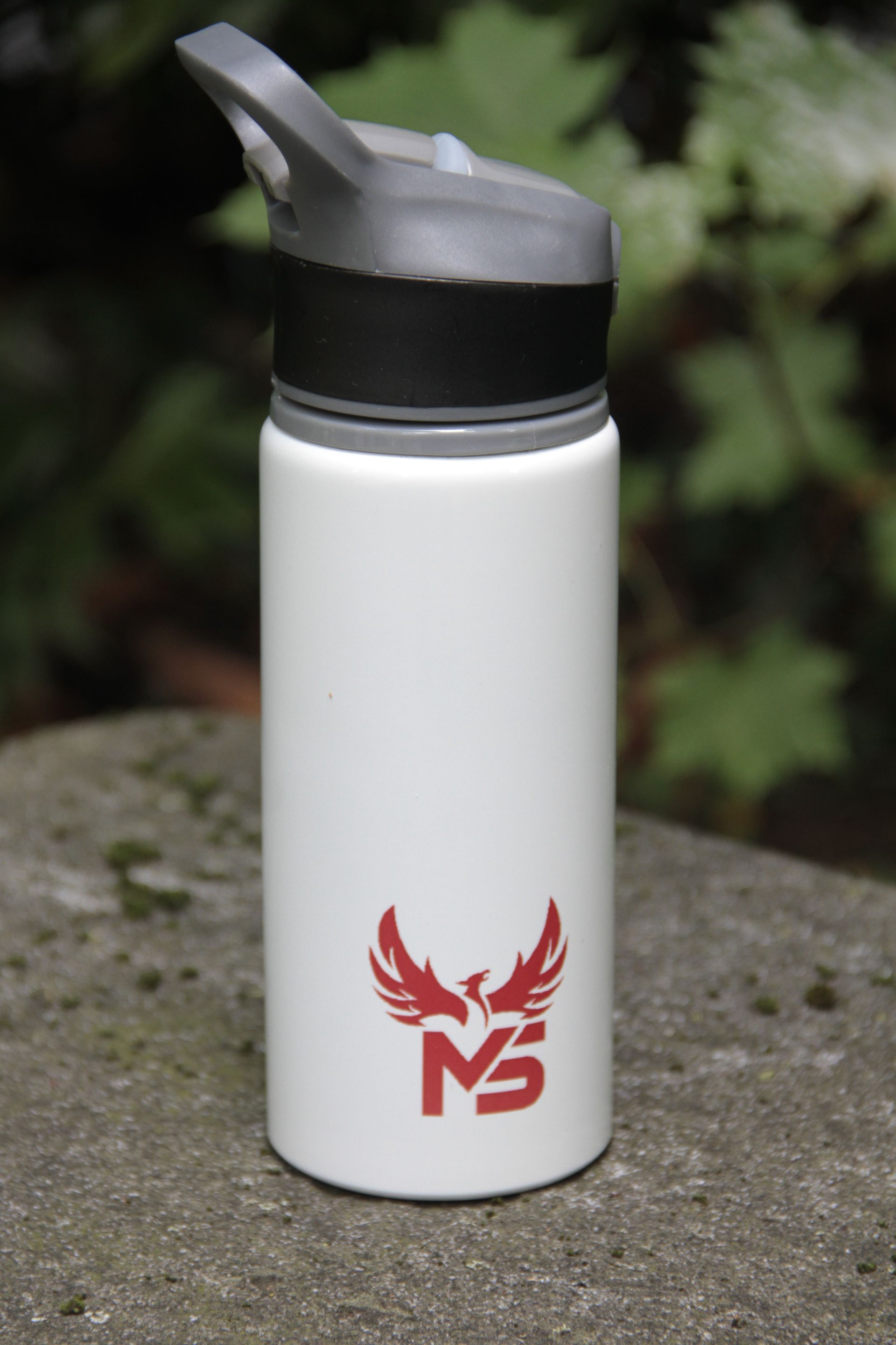 Bouteille d'eau blanche avec bouchon noir et logo rouge posée sur une surface en pierre à l'extérieur