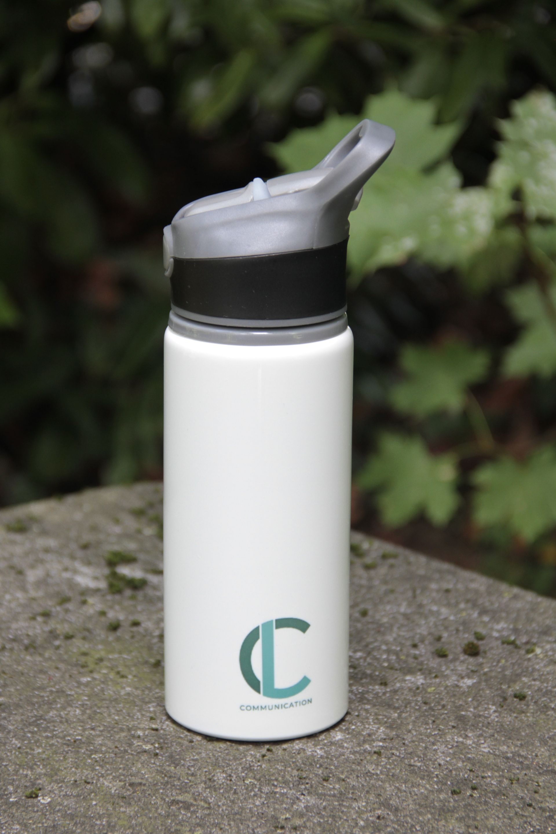 Bouteille d'eau isotherme blanche avec bouchon noir et logo turquoise posée sur une surface en pierre à l'extérieur