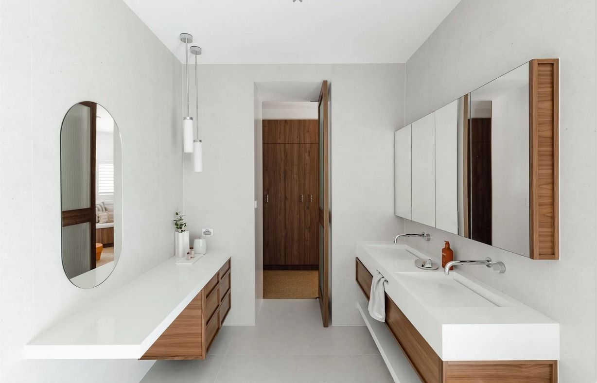 Modern white bathroom with floating wood vanities, twin sinks, oval and rectangular mirrors, and a wooden door. — PKJ Design in Unanderra, NSW