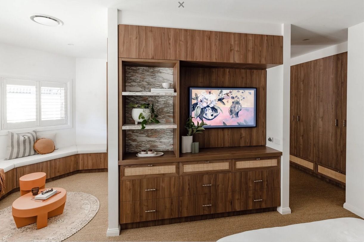 A modern bedroom divider featuring a walnut-wood media console with shelving, facing a cozy window seat and round table. — PKJ Design in Unanderra, NSW
