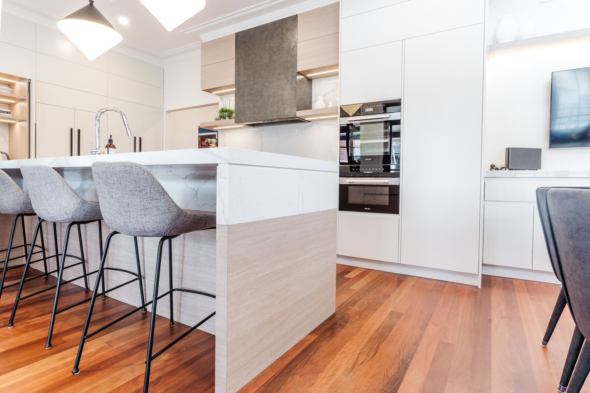 Modern Kitchen With White Cabinets, Wood Floors, and Island Stools — PKJ Design in Unanderra, NSW