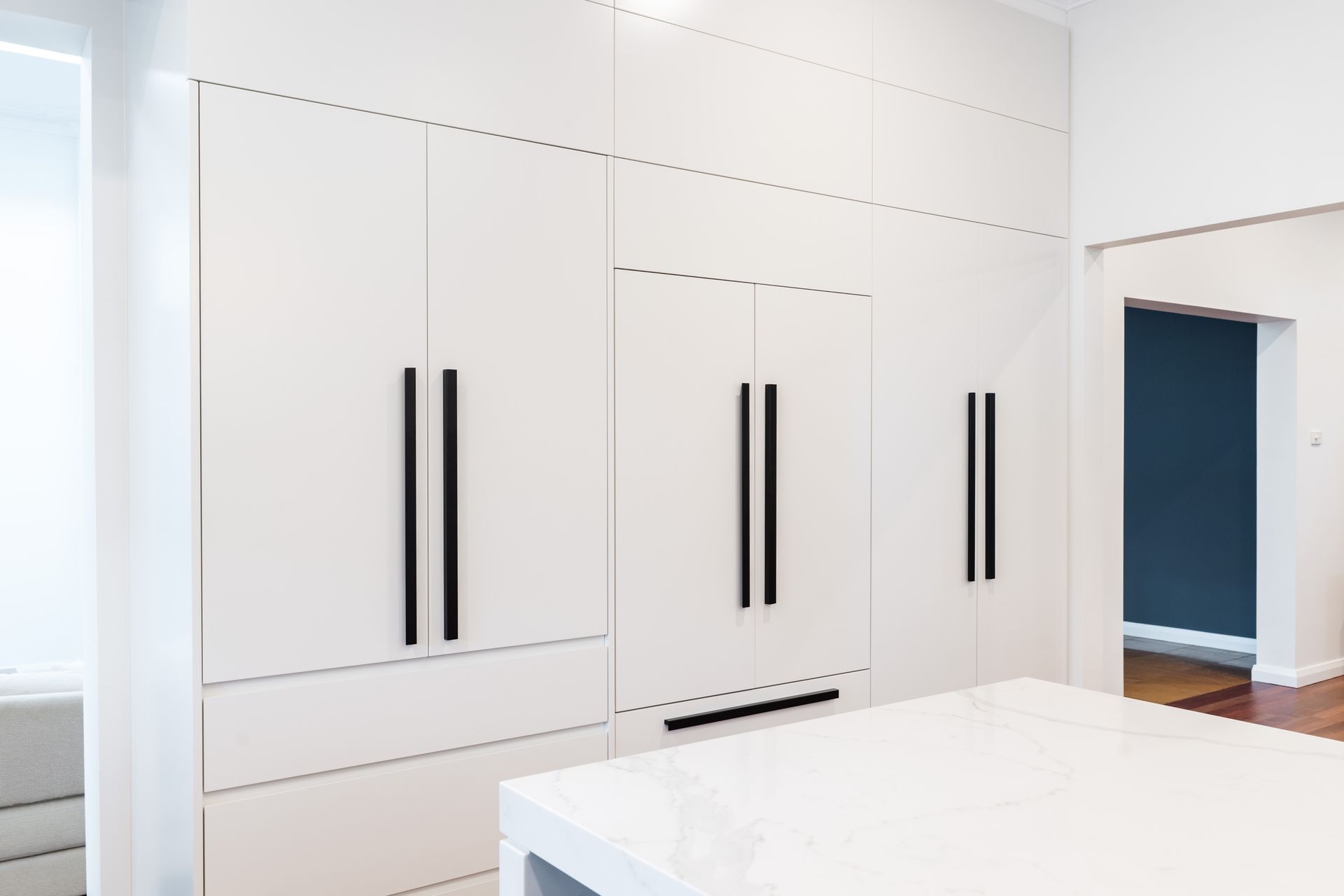 Modern White Kitchen Cabinets With Black Handles and an Island — PKJ Design in Unanderra, NSW
