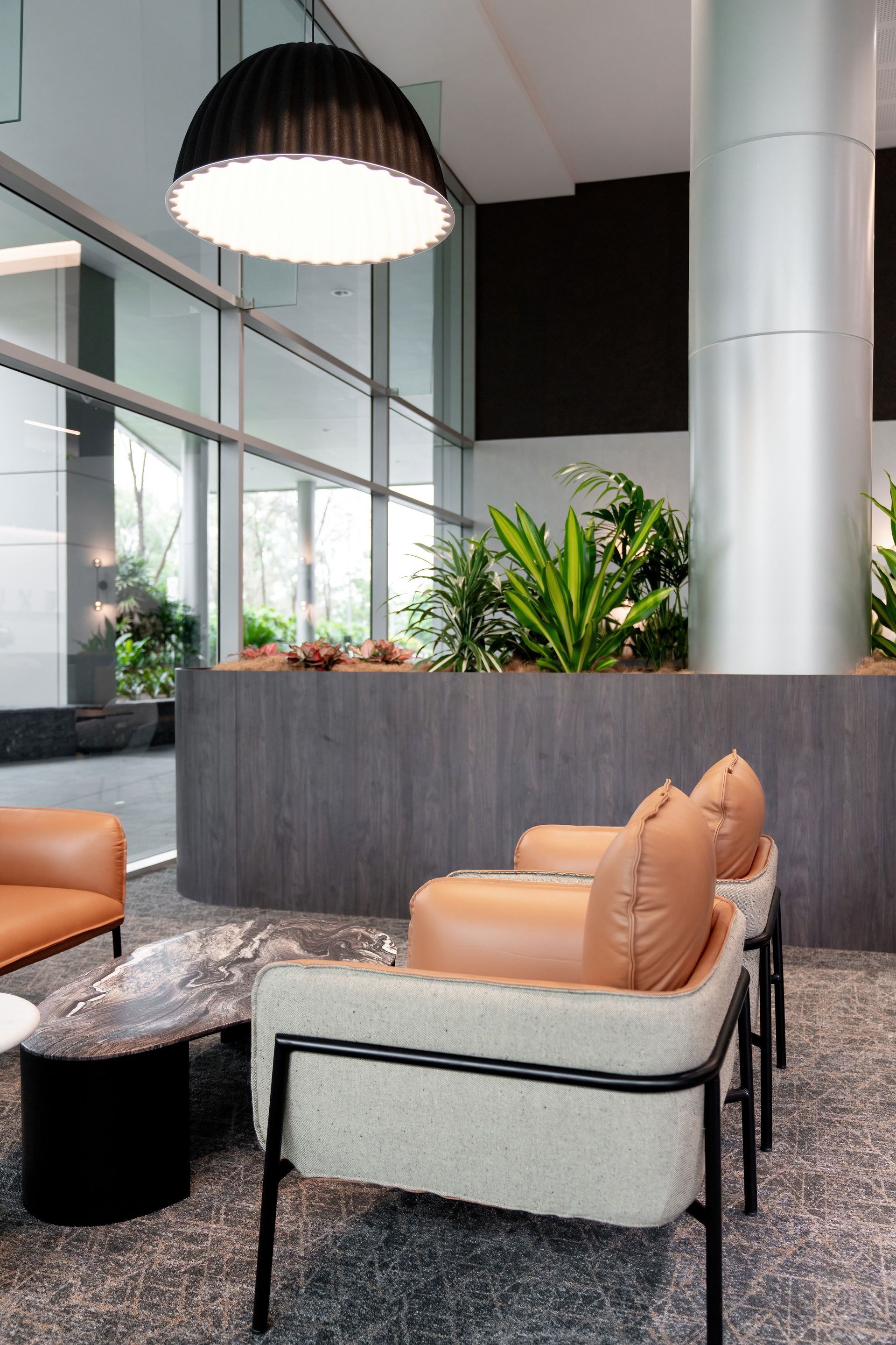 Modern lobby seating area with tan chairs, a marble table, plants, and large windows — PKJ Design in Unanderra, NSW