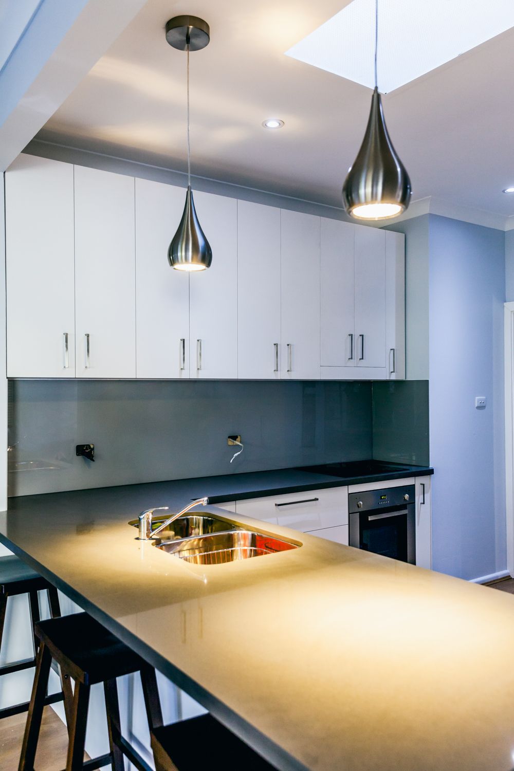 Kitchen With Cabinets, Dark Backsplash, Island, and Pendant Lights — PKJ Design in Unanderra, NSW