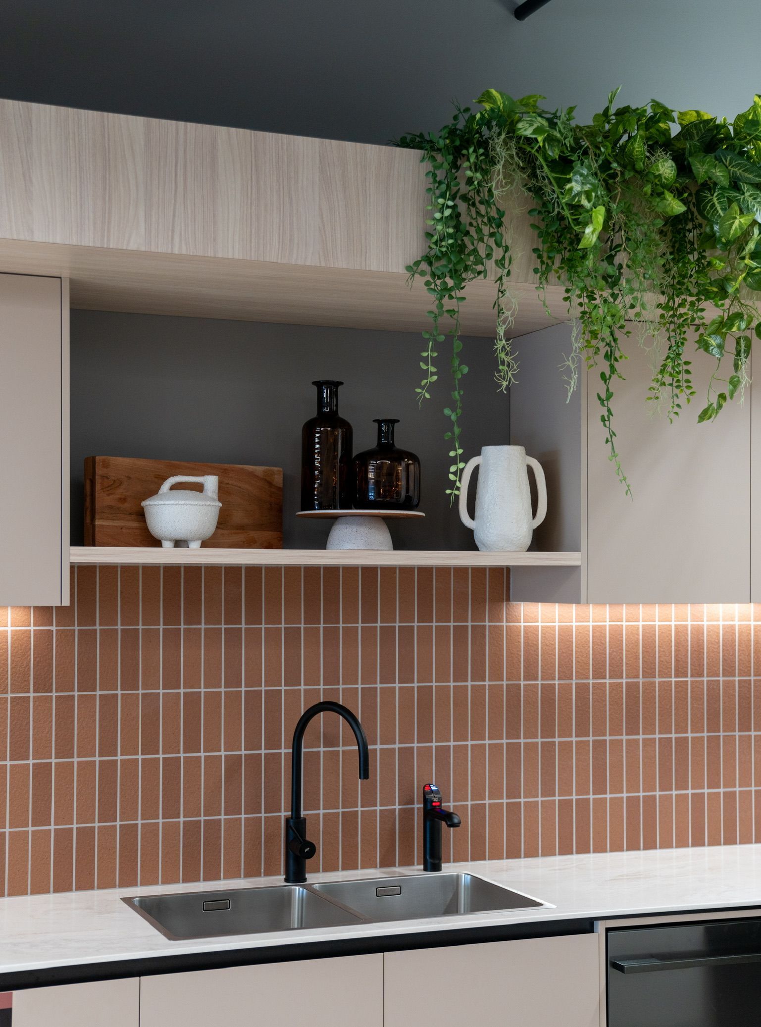 Modern kitchen sink with copper tile backsplash, open shelves, and hanging green plants — PKJ Design in Unanderra, NSW 