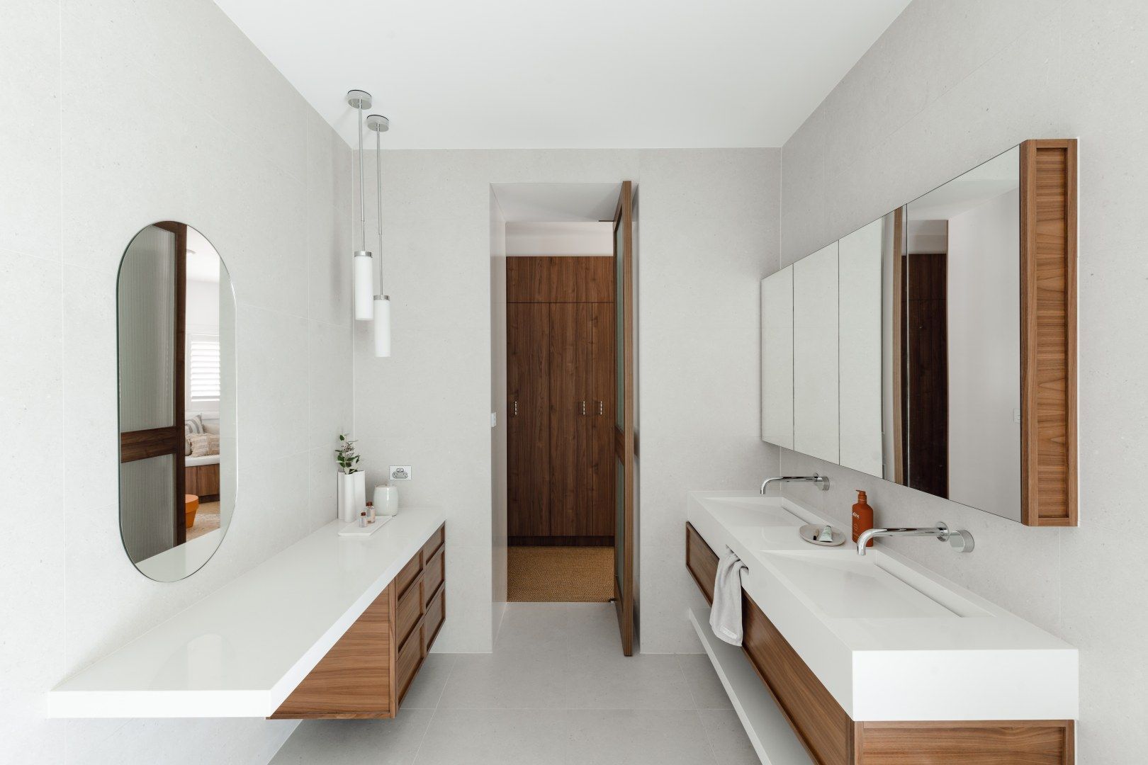 Modern white bathroom with double sinks, long countertop, mirrors, and a wooden door. — PKJ Design in Unanderra, NSW