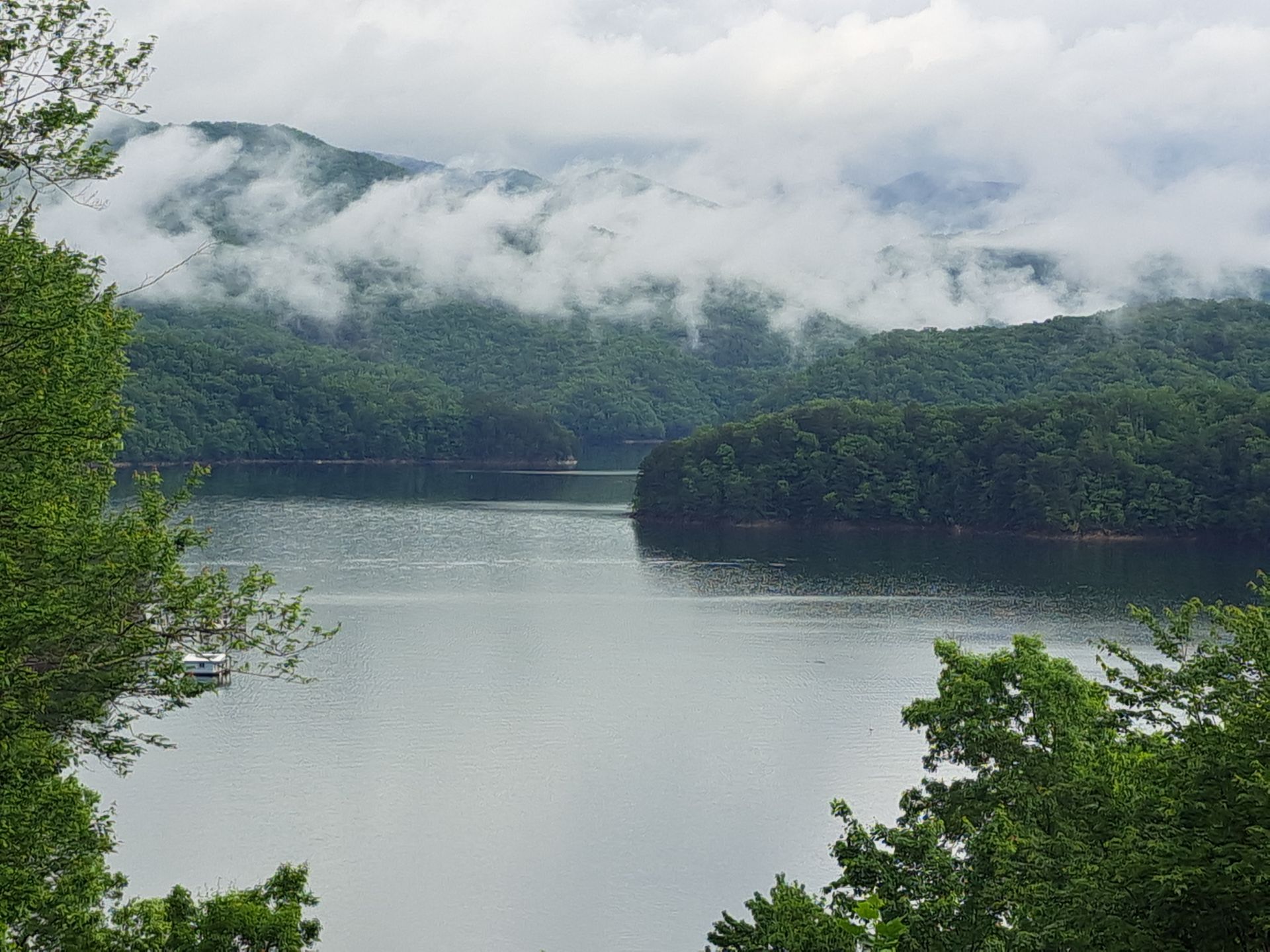 A lake surrounded by trees and mountains on a cloudy day.