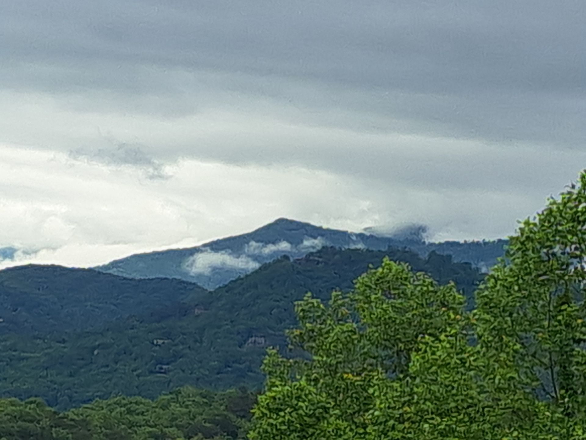 A view of a mountain range with trees in the foreground and clouds in the sky.