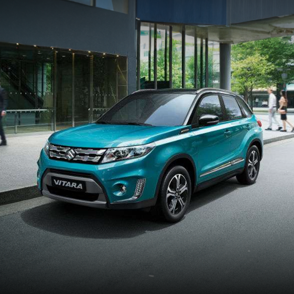 Um suzuki vitara azul está estacionado em frente a um prédio